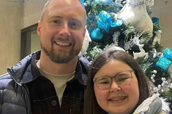 Мужчина и девушка улыбаются у елки с голубыми украшениями.