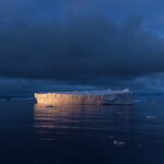 Пейзаж арктики: айсберг на фоне тёмного неба отражается в спокойной воде.