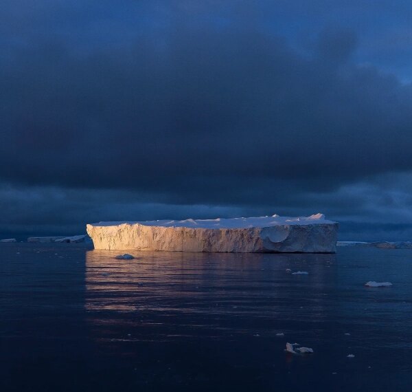 Пейзаж арктики: айсберг на фоне тёмного неба отражается в спокойной воде.