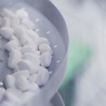 Белые таблетки на конвейере в процессе производства медикаментов.