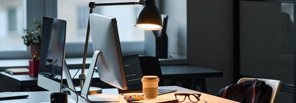Современный офис с компьютером и лампой, очки и кофе на столе.