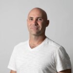 Мужчина в белой футболке на сером фоне.