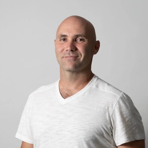 Мужчина в белой футболке на сером фоне.