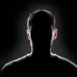 Силуэт неизвестного человека на темном фоне, контровой свет, загадочная атмосфера.
