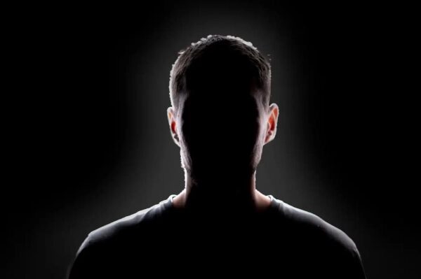 Силуэт неизвестного человека на темном фоне, контровой свет, загадочная атмосфера.