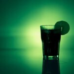 Коктейль с лимоном в стакане на зелёном фоне, освежающий напиток.