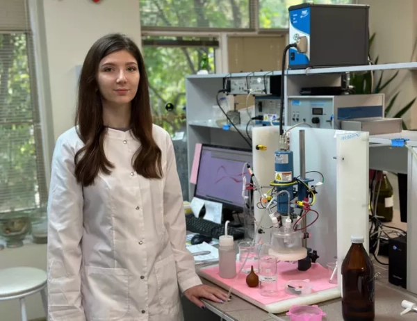 Женщина в лабораторном халате рядом с научным оборудованием в лаборатории.