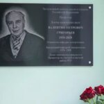 Памятная табличка заслуженному деятелю науки Валентину Григорьеву с цветами на фоне.
