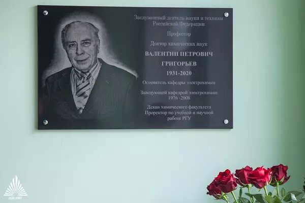 Памятная табличка заслуженному деятелю науки Валентину Григорьеву с цветами на фоне.