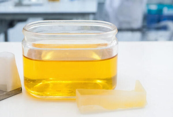Банка с жёлтой жидкостью на светлом столе, рядом прозрачные куски воска.
