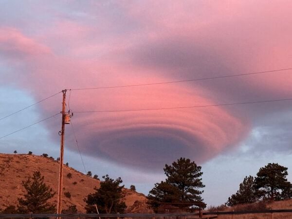 Розовое лентообразное облако на закате над холмом с деревьями и столбом.