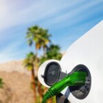 Электромобиль на зарядке на фоне пальм и голубого неба.