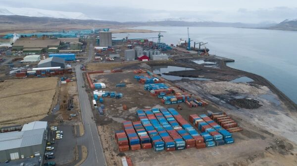 Промышленный порт с контейнерами и кранами у моря на фоне гор.