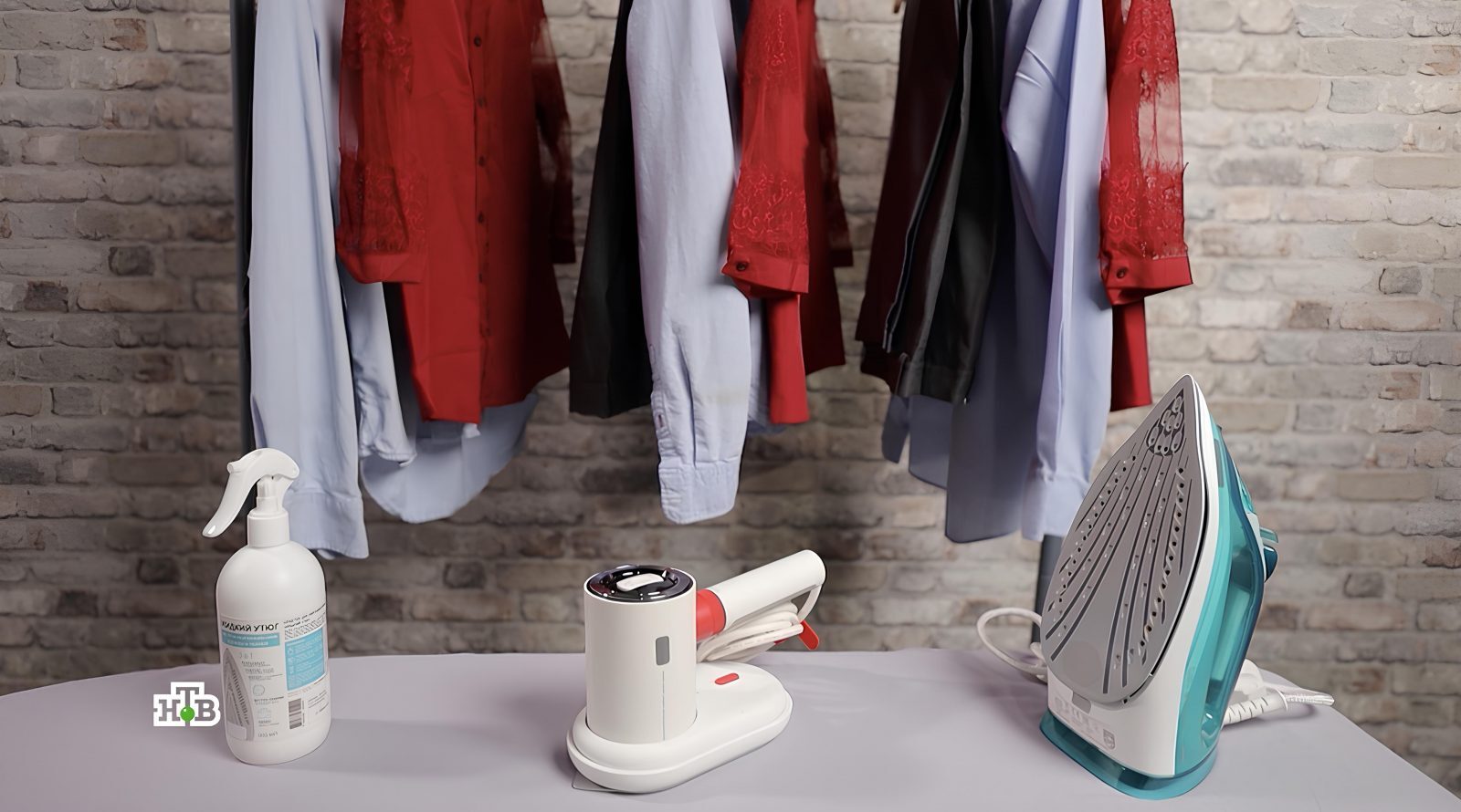 Рубашки на вешалке, утюг, отпариватель и спрей на фоне кирпичной стены.