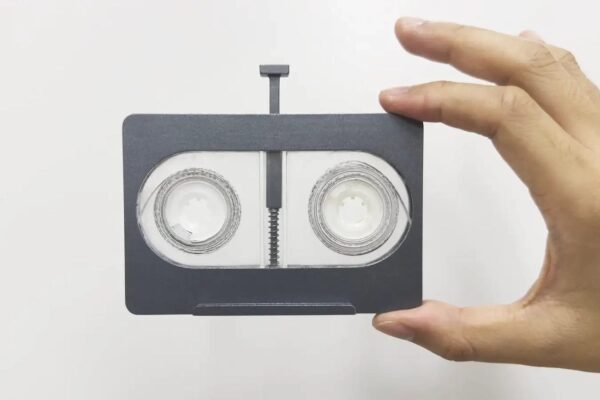 Рука держит аудиокассету уникального дизайна на белом фоне.
