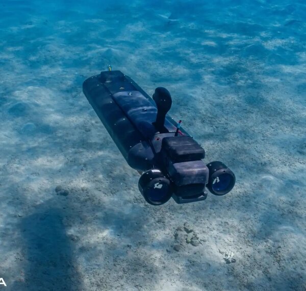 Подводный дрон в голубой воде океана делает снимки морского дна.