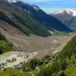 Горная долина с затопленной деревней и тающими снегами на фоне.