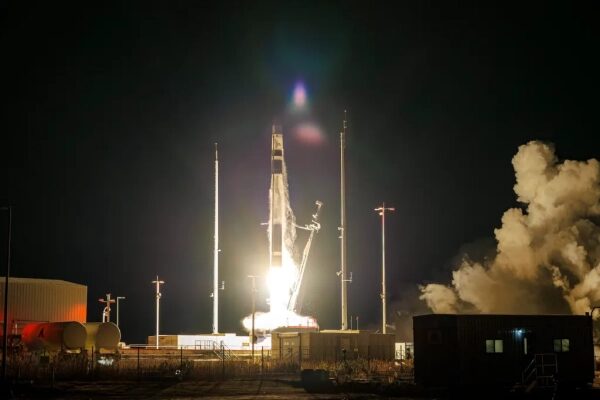 Ночной запуск ракеты в космос с освещенной площадки и дымом на заднем плане.