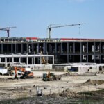 Строительная площадка с кранами и спецтехникой на фоне недостроенного здания.