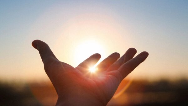 Рука на фоне восходящего солнца, символ надежды и начала нового дня.