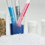 Пластиковые гранулы разных цветов в пробирках и контейнерах на белом фоне.