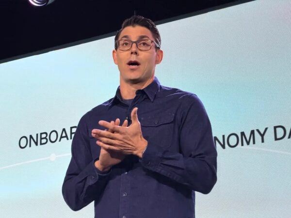 Человек в очках на сцене, выступление с презентацией на конференции.