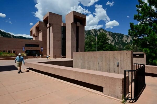 Современное здание с красным фасадом на фоне гор и синего неба.