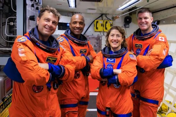 Астронавты в оранжевых скафандрах на космическом корабле, улыбаясь.