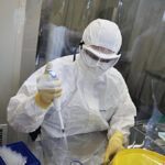 Учёный в защитном костюме работает с пробирками в лаборатории.