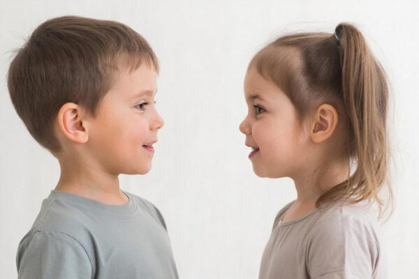 Дети стоят лицом друг к другу в нейтральной одежде на светлом фоне.