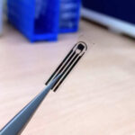 Прозрачный микрочип в пинцете на лабораторном столе, технология, микроэлектроника.