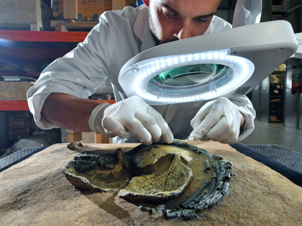 Археолог изучает древний артефакт под увеличительным стеклом в лаборатории.