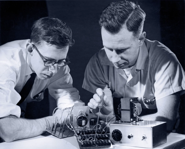Фрэнк Розенблатт (слева) и Чарльз Уайтман (справа) наклоняются над компьютером — единицей персептрона — с отверткой.