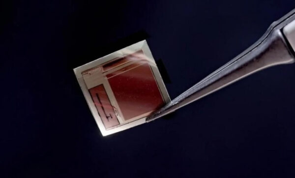 Миниатюрная солнечная панель на фоне тёмном фоне, держится пинцетом.