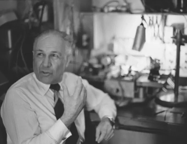 Человек в рубашке и галстуке сидит в научной лаборатории с оборудованием.