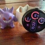 Фиолетовая фигурка рядом с умными часами на деревянной поверхности.