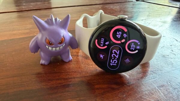 Фиолетовая фигурка рядом с умными часами на деревянной поверхности.