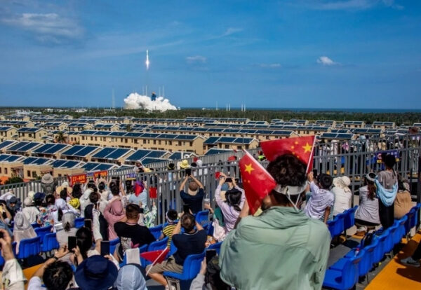 Запуск ракеты в ясное небо, зрители наблюдают за стартом с трибун.