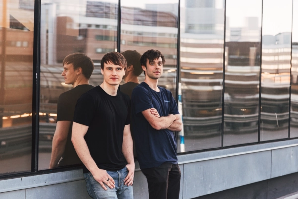 Два человека в черных футболках стоят рядом с отражающим стеклом на фоне городского пейзажа.