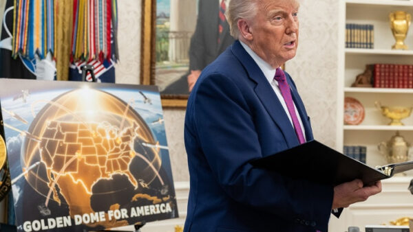 Человек с папкой выступает в офисе возле постера США, посвящённого проекту "Golden Dome".