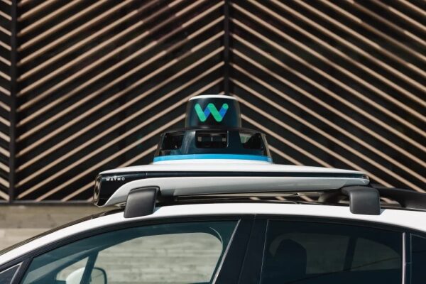 Автомобиль Waymo с лидаром на крыше у геометрической стены.