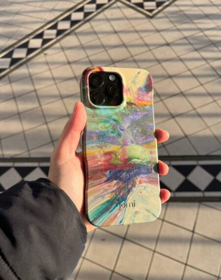 Смартфон в ярком разноцветном чехле в руке на фоне плиточного пола.