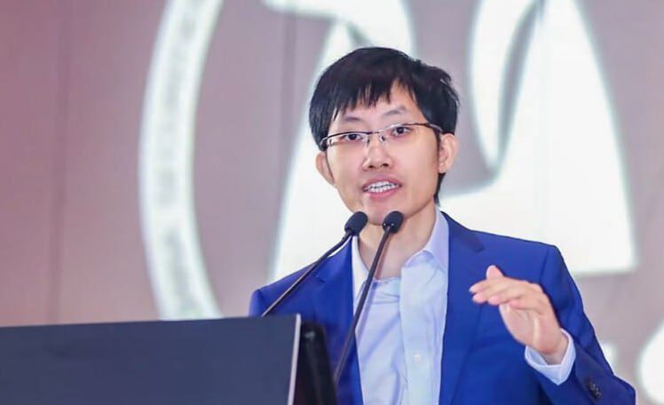 Человек в синем костюме выступает на конференции с микрофоном.