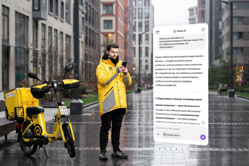 Курьер в желтой куртке с электровелосипедом и смартфоном на улице зимой.