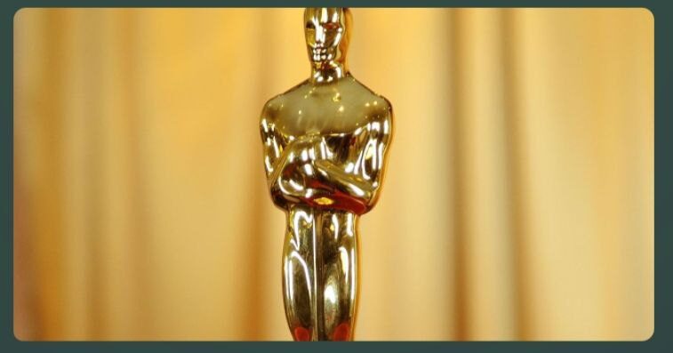 Золотая статуэтка Оскар на фоне размытых занавесок.