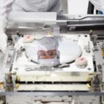 Инженеры в защитных костюмах работают с полупроводниковым оборудованием в лаборатории.