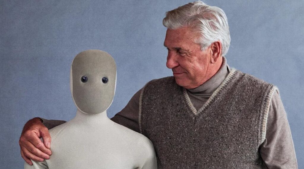 Старший мужчина обнимает робота с нейтральным лицом на сером фоне.