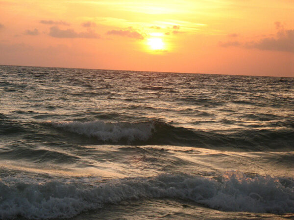 Закат над морем, волны на воде, солнечный диск над горизонтом, оранжевое небо.