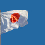 Флаг Японии развевается на ветру на фоне голубого неба.