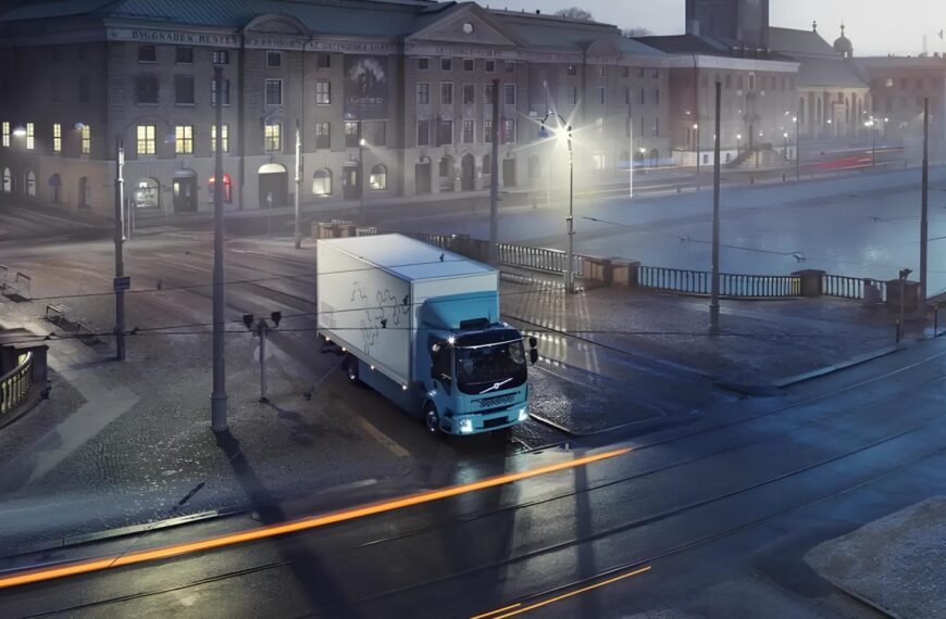 Грузовик ночью на городской улице с архитектурным зданием на заднем плане.